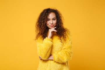 Stunning young african american girl in fur sweater posing isolated on yellow orange wall background in studio. People sincere emotions lifestyle concept. Mock up copy space. Put hand prop up on chin.