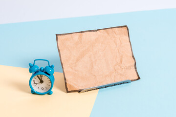 Mini size alarm clock beside a Paper sheet placed tilted on pastel backdrop