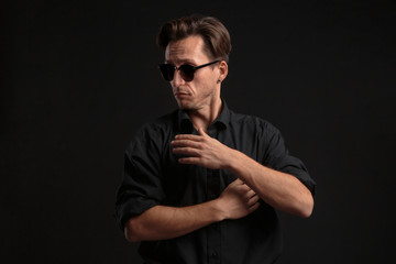 Fototapeta na wymiar Confident stylish bussinesman in black eyeglasses buttoning up balck shirt isolated over black background.