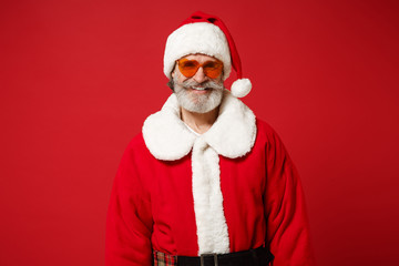 Smiling elderly gray-haired mustache bearded Santa man in Christmas hat, sunglasses posing isolated on red background in studio. Happy New Year 2020 celebration holiday concept. Mock up copy space.