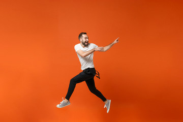 Fototapeta na wymiar Cheerful young man in casual white t-shirt posing isolated on orange wall background. People lifestyle concept. Mock up copy space. Having fun, fooling around, jumping, pointing index fingers aside.