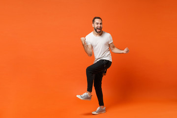 Fototapeta na wymiar Joyful happy young man in casual white t-shirt posing isolated on orange wall background studio portrait. People sincere emotions lifestyle concept. Mock up copy space. Clenching fists like winner.