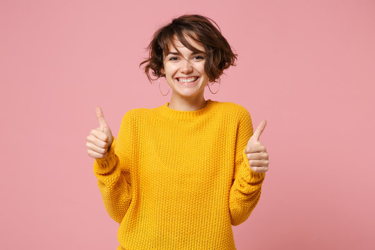 Cheerful young brunette woman girl in yellow sweater posing isolated on pastel pink wall background, studio portrait. People sincere emotions lifestyle concept. Mock up copy space. Showing thumbs up.