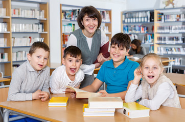 Smiling pupils with teacher sitting in school library