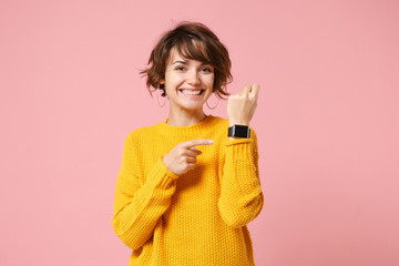 Smiling young brunette woman girl in yellow sweater posing isolated on pink wall background studio...
