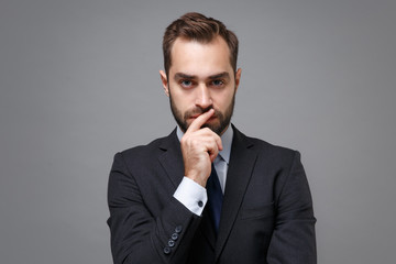 Pensive young bearded business man in classic black suit shirt tie posing isolated on grey wall background. Achievement career wealth business concept. Mock up copy space. Put hand prop up on chin.