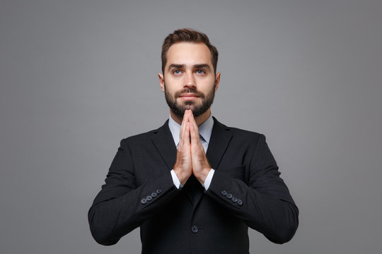 Young business man in classic black suit shirt tie posing isolated on grey background studio portrait. Achievement career wealth business concept. Mock up copy space. Holding hands folded in prayer.