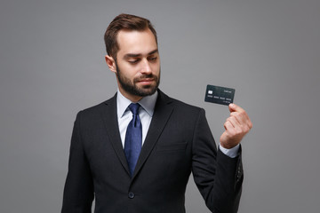 Handsome young business man in classic black suit shirt tie posing isolated on grey wall background in studio. Achievement career wealth business concept. Mock up copy space. Holding credit bank card.