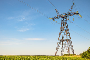 Power Transmission Tower. Air hi-voltage electric line supports at cornfield under blue sky.