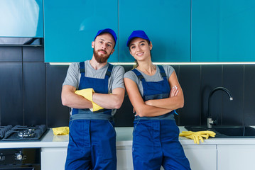 Attractive man and pretty woman in workwears posing on the camera in the contemporary cuisine with detergents