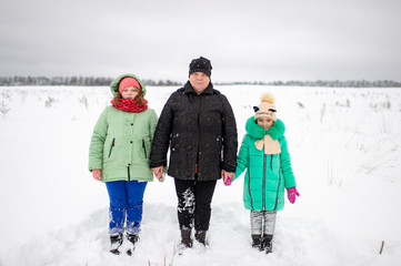 Outdoor portrait of grandmother holding hands of her two granddaughters standing by two sides of her in snowy winter field