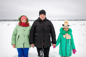 Outdoor portrait of grandmother holding hands of her two granddaughters standing by two sides of her in snowy winter field