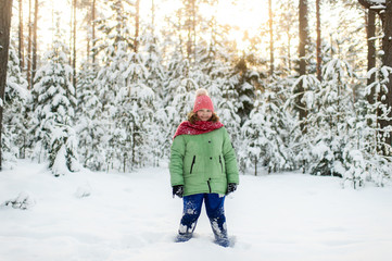 Fototapeta na wymiar Portrait of plump funny girl in winter clothes posing for camera in snowy forest.