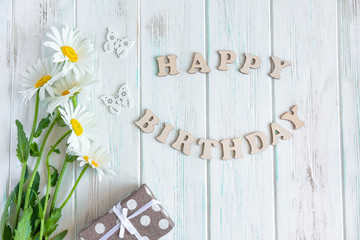 Happy birthday greeting card with camomile flowers on white wooden background. Flat lay, top view.