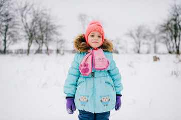 Fototapeta na wymiar Positive little girl looking standing in snowy field and looking at camera