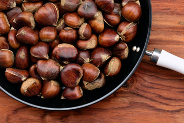 Obraz premium Many brown onesfresh and raw sweet chestnuts in a pan with white handle on wooden background