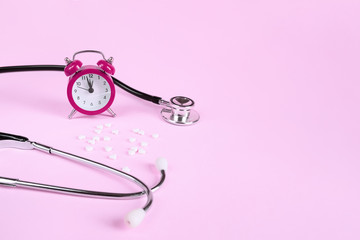 Pills, stethoscope and alarm clock on a pink background with copy space. Medical concept - its time to take medicine.