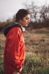 Naklejka premium Young woman standing with raincoat and headphones on the field
