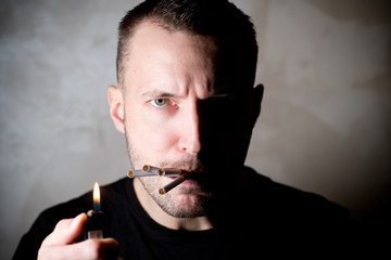 a man with a half-lit face looks skeptical and cigarettes stick out from his mouth