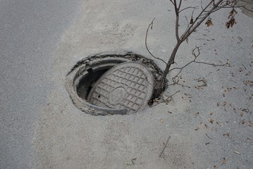 broken iron sewer manhole in the pit on the gray asphalt of the road