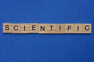 word scientific made from brown wooden letters lies on a blue table