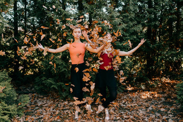 Portrait of two elegant ballerinas in black leggings pants, tutu and pointe shoes throwing up leaves and posing with happy smiling faces.