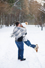 Fototapeta na wymiar Young stylish couple in love have fun while walking on the snowy winter park. Handsome young man holds his beautiful girl on the hands.