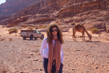 Woman posing in frond of a jeep and a camel in the Jordan desert