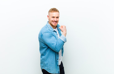 young blonde man wearing jeans shirt feeling happy, satisfied and powerful, flexing fit and...