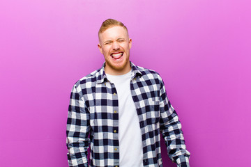 young blonde man with squared shirt with cheerful, carefree, rebellious attitude, joking and...