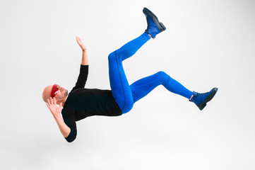 Side view of stylish man in futuristic red glasses and blue tights lying in air against white studio background with legs and hands apart