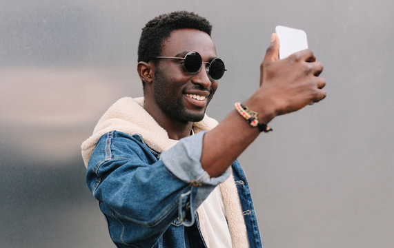 Portrait close up of happy smiling african man taking selfie picture by smartphone on gray wall background