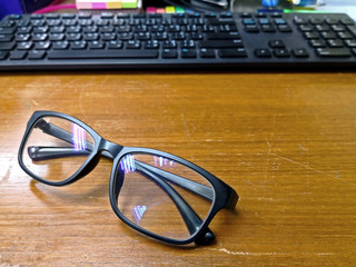 Eyeglasses place on old wooden desk with blurred computer keyboard background.