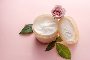 Obraz na płótnie Canvas The jar of skin care or body care cream with lid and rose flower with leaves on pink background