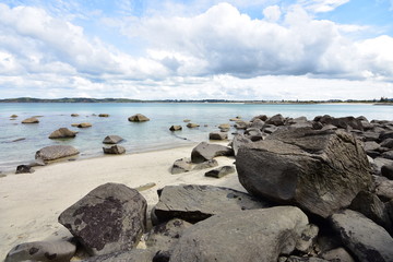 Sandy beach with large stones both on shore and in clear shallow water.