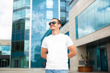 Adult man in white blank t-shirt standing near modern building