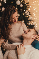 Lovely couple in sweaters hugging and celebrating new year in front of Christmas tree in decorated interior.