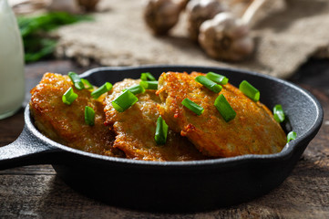 potato pancakes with meat and sour cream lie in a pan seasoned with greens, onions and dill. frying pan with pancakes stands on old wooden background