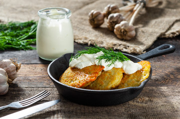 potato pancakes with meat and sour cream lie in a pan seasoned with greens, onions and dill. frying pan with pancakes stands on old wooden background