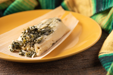Tamale with spinach in la hoja de maiz corn husk on a yellow plate styled with a serape and reclaimed wood.