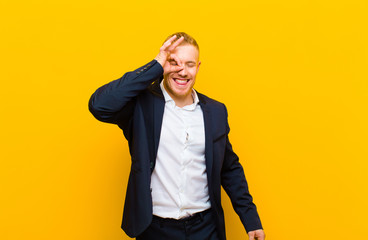 young blond businessman smiling happily with funny face, joking and looking through peephole,...