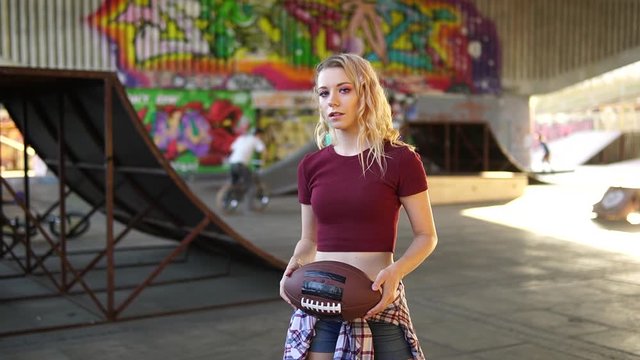 Young attractive woman plays with an american football ball and practicing or learning how to thrown it in a city skate park