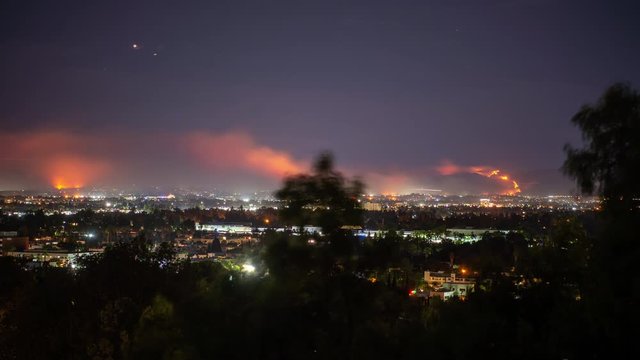 Timelapse forest fire on mountain range of residential neighborhood at night has planes dump water and smoke spreads.