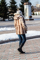 A girl in a fur coat walks along the street, autumn cold day.