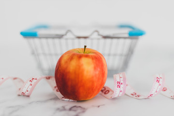 diet and nutrition, red apple with measuring tape and grocery store shopping basket