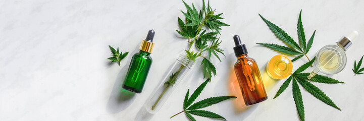 Various glass bottles with CBD oil, THC tincture and hemp leaves on a marble background. Flat lay,...