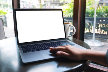 Mockup image of a hand using and touching on laptop touchpad with blank white desktop screen with coffee cup on the table
