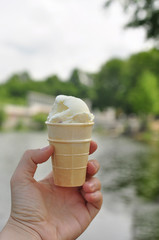 hand of fair skin holds a waffle glass of white milk ice cream on a background of water and greens...