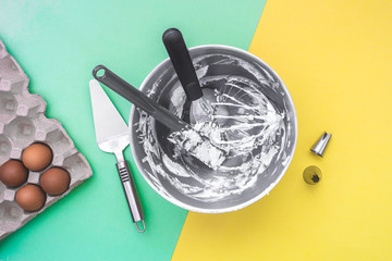 Cake baking utensils in mixer bowl after cake making, nozzles, raw eggs on flat lay green yellow background