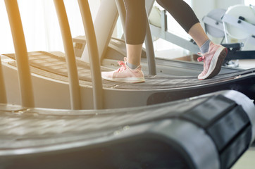 Woman runner feet exercising to running on treadmill in gym with warm light, She is jogging, fitness and jog workout wellness concept, selective focus